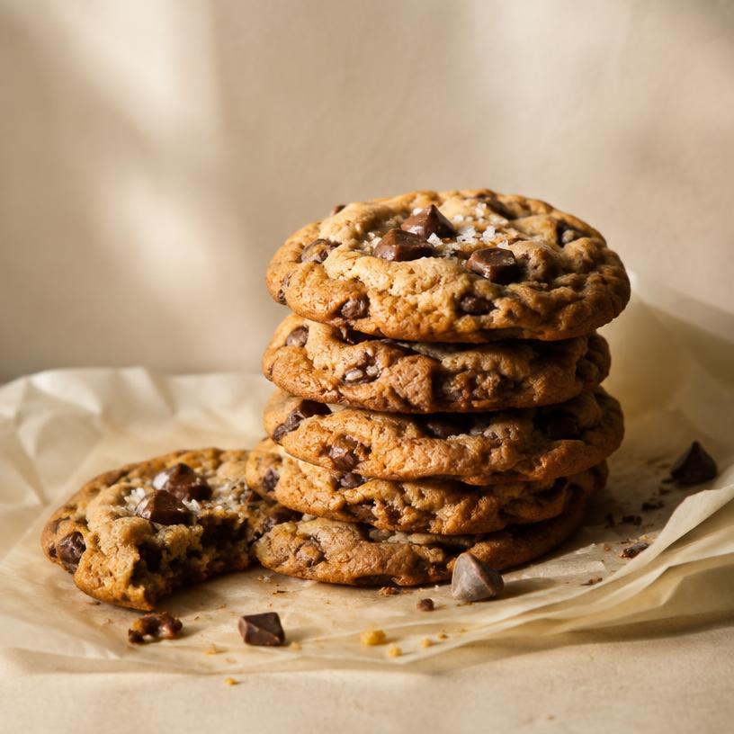 Brown butter chocolate chip cookies stacked on parchment with flaky sea salt